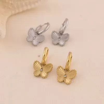Brincos com pendente de borboleta dourados e prateados sobre fundo creme