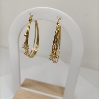 Brincos de argola dourados com estrela e pedras em suporte branco e base de madeira