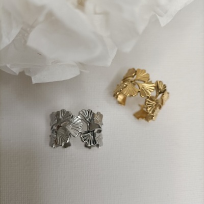Anéis de folhas em metal prateado e dourado sobre fundo branco com tecido branco desfocado