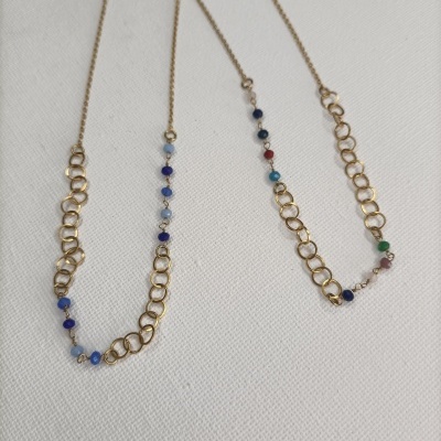 Colares dourados com elos e contas coloridas sobre tecido branco