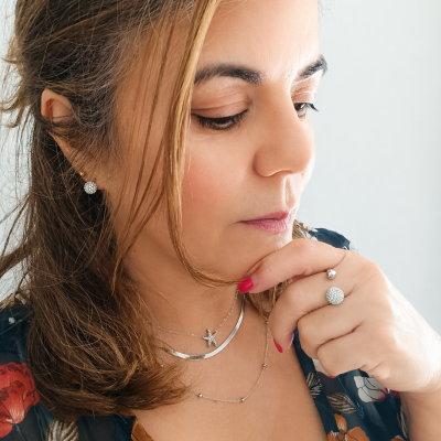 Mulher com colar, anel e brincos prateados e blusa floral azul escura