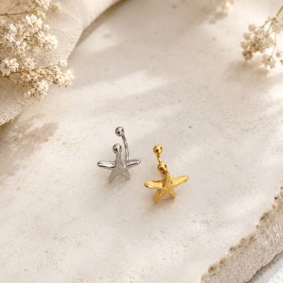 Brincos estrela-do-mar prateado e dourado sobre superfície clara com flores secas