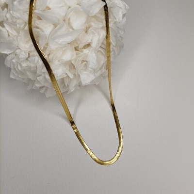 Colar dourado liso colocado em fundo branco com decoração de papel branco.