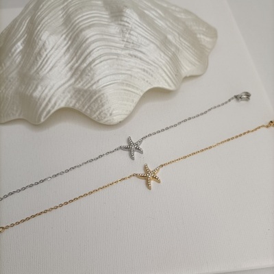 Duas pulseiras finas com pendentes de estrela-do-mar e pequenos cristais sobre fundo branco.