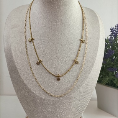 Duas gargantilhas douradas com pendentes florais em suporte de joias cinza