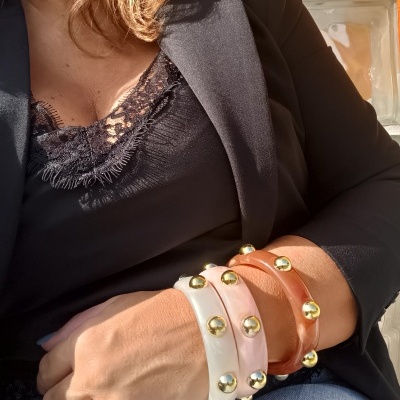 Pulseras coloridas com detalhes dourados no braço de pessoa com roupa preta e calças de ganga azuis.