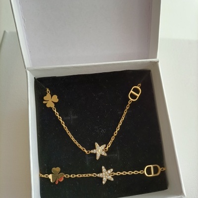 Imagem de conjunto de joias douradas com pingentes de trevo e estrela em estojo branco.