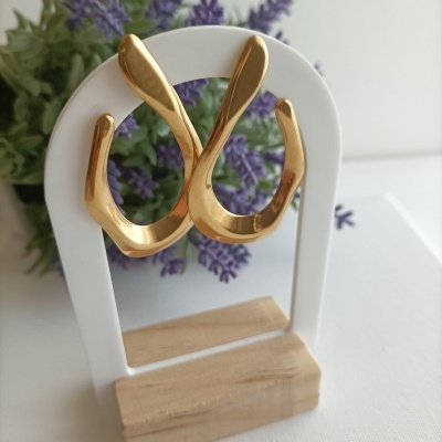 Brincos dourados curvos pendurados em moldura branca com base de madeira