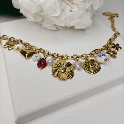 Pulseira dourada com pendentes variados sobre suporte branco