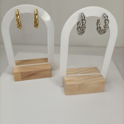 Brincos argola torcidos dourados e prateados em suportes brancos com base de madeira clara