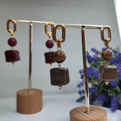 Brincos pendentes com pedras castanhas e vermelhas em suportes de madeira