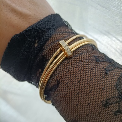 Pulseira dourada com pedras sobre luva preta de renda