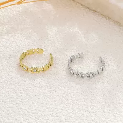 Dois anéis entrelaçados, dourado e prateado, com pequenos cristais, sobre fundo bege texturado.