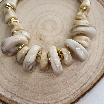 Colar com pedras bege e marfim e elementos dourados sobre disco de madeira