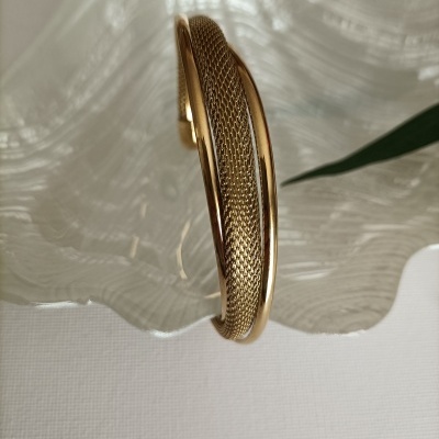 Pulseira dourada com malha metálica central sobre prato de vidro texturizado