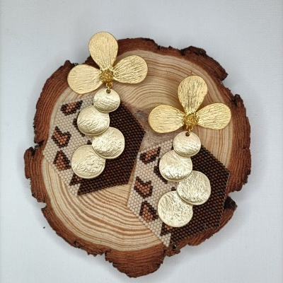 Brincos dourados pendurados em madeira decorativa com padrão geométrico