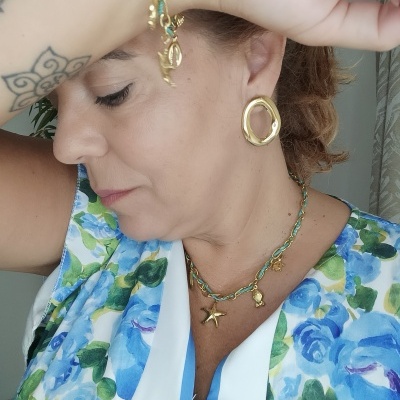 Mulher com joias douradas e vestido floral azul e verde