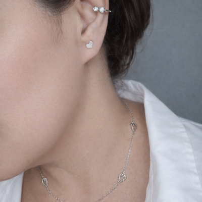 Colar prateado com corações, brinco coração pequeno e argola com pedras na orelha de mulher com camisa branca