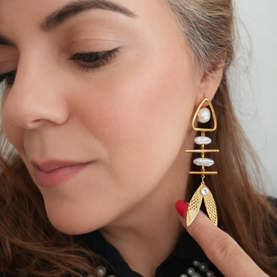 Brinco dourado pendente com pérolas e detalhes decorativos usado por mulher