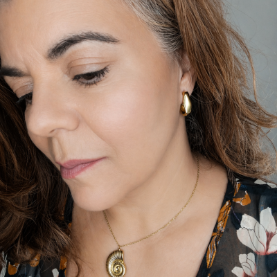 Colar e brinco dourados em forma de concha usados por mulher com blusa floral.