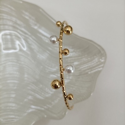 Pulseira dourada com bolas e pérolas sobre vidro ondulado