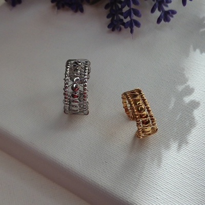 Dois anéis de arame em metal prateado e dourado com esferas, sobre superfície branca com sombra de planta.