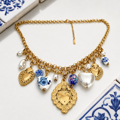 Colar dourado com pendentes de corações, pérolas e contas azuis e brancas sobre azulejos decorativos
