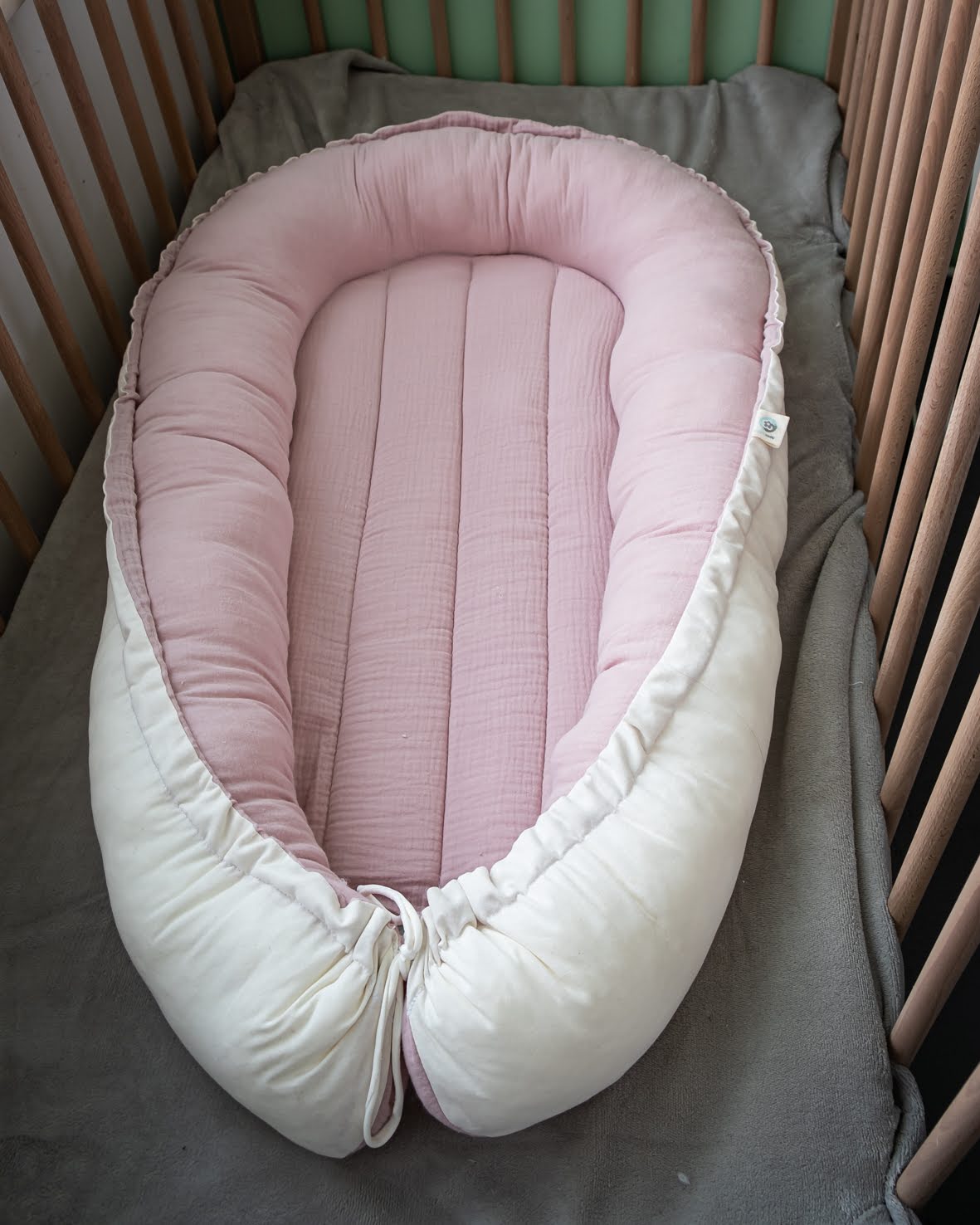Ninho Cru ninho de bebé rosa claro e branco dentro de berço de madeira sobre tecido cinza
