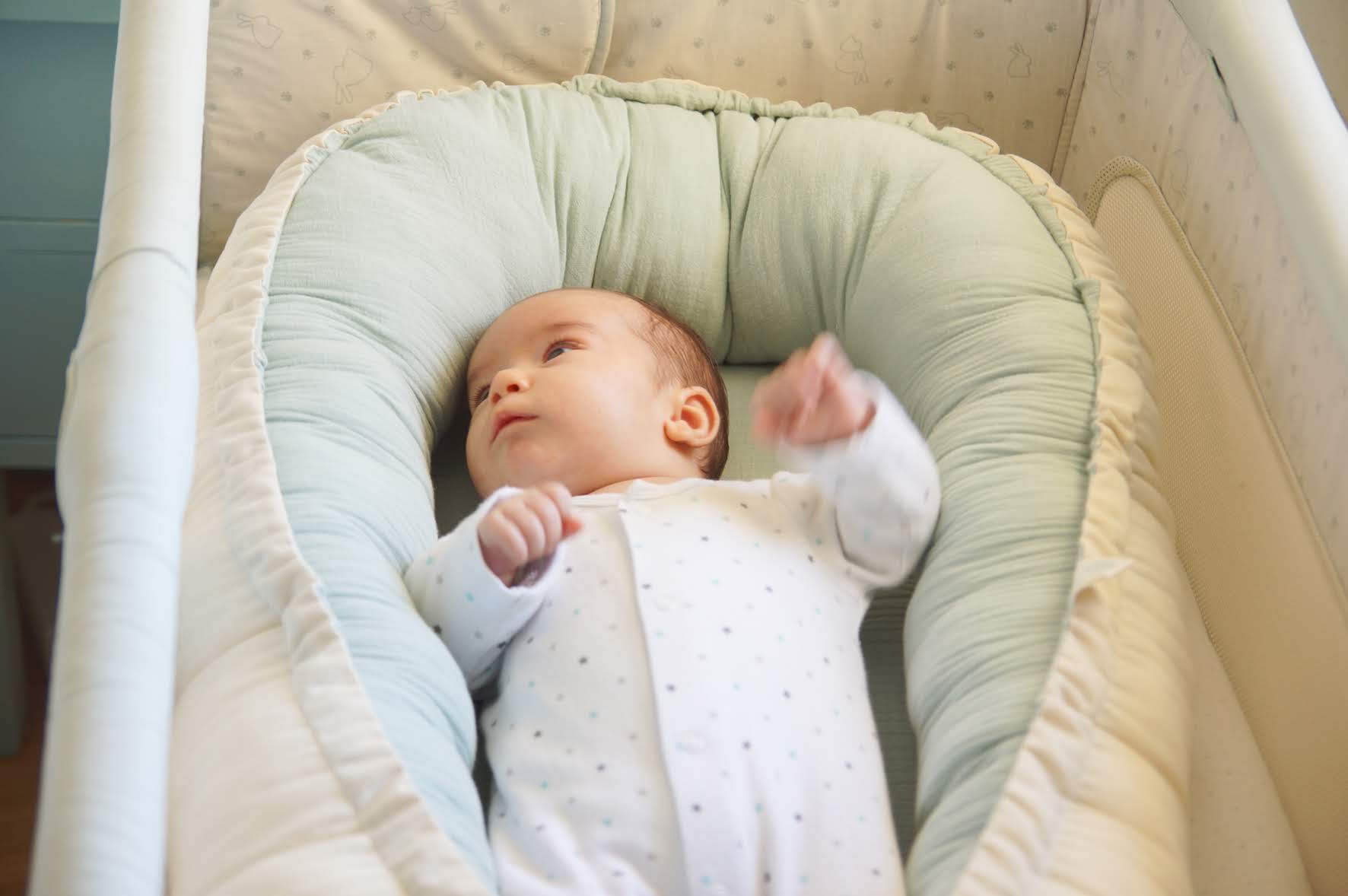 Ninho Cru Bebé em pijama branco com ninho acolchoado verde em berço branco