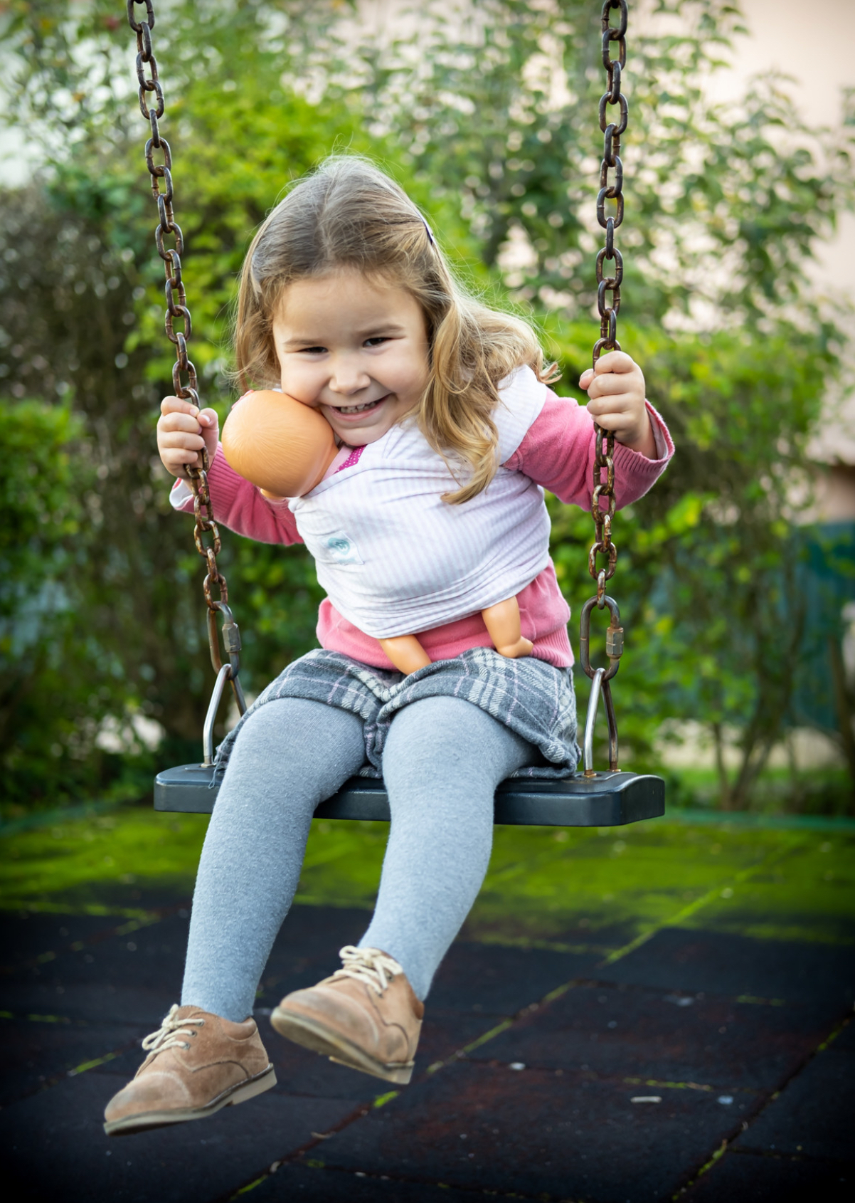 ISling4kid - Porta-bonecas Criança loira num baloiço a brincar com boneca num parque