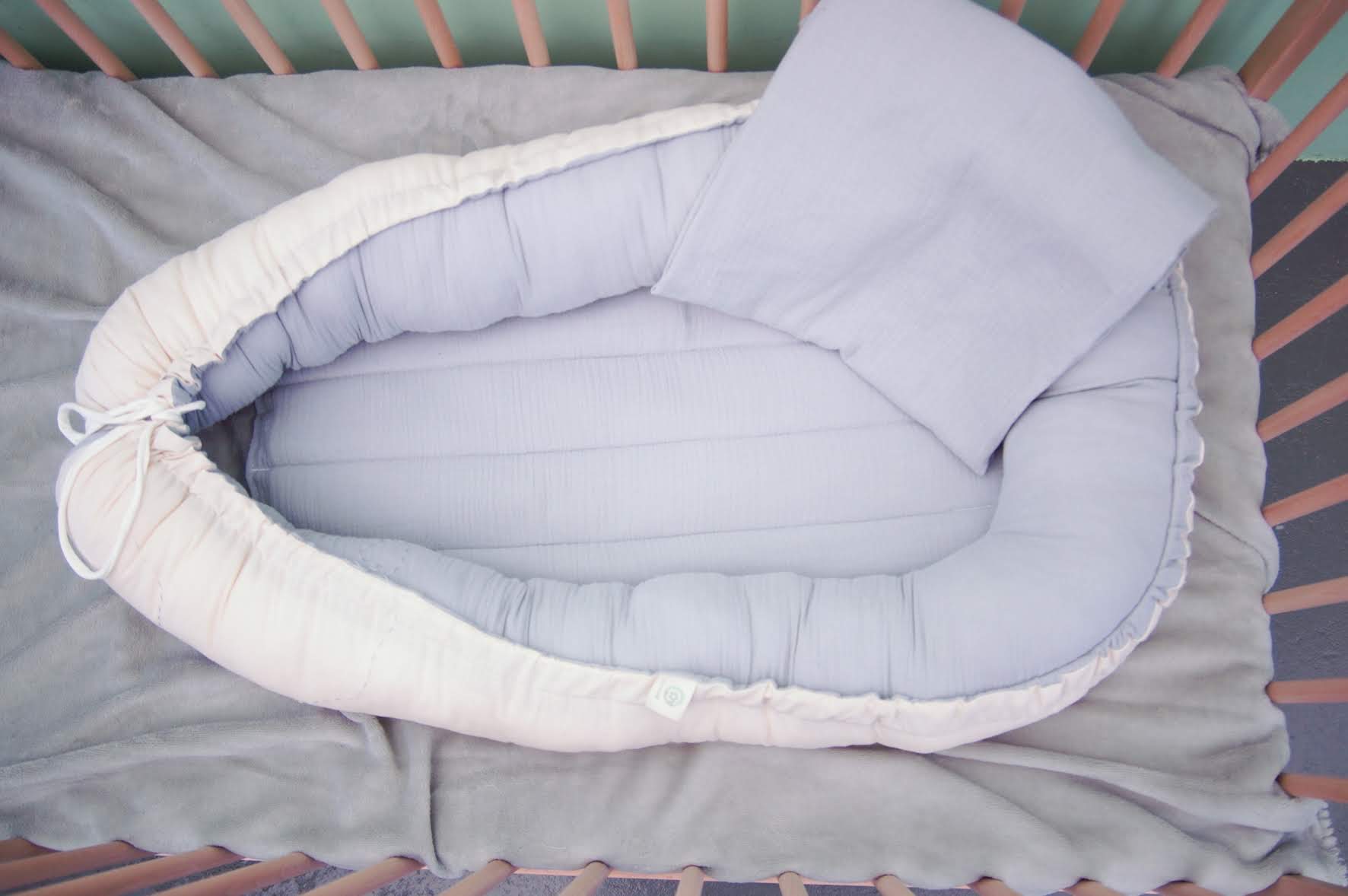 Ninho Cru Ninho de bebé cinza claro e branco num berço cor-de-rosa