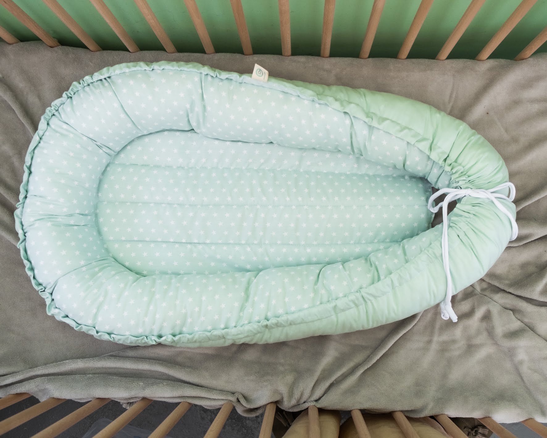 Ninho liso com padrão Ninho de bebé verde claro com bolinhas brancas e laterais acolchoadas numa cama de grades de madeira clara