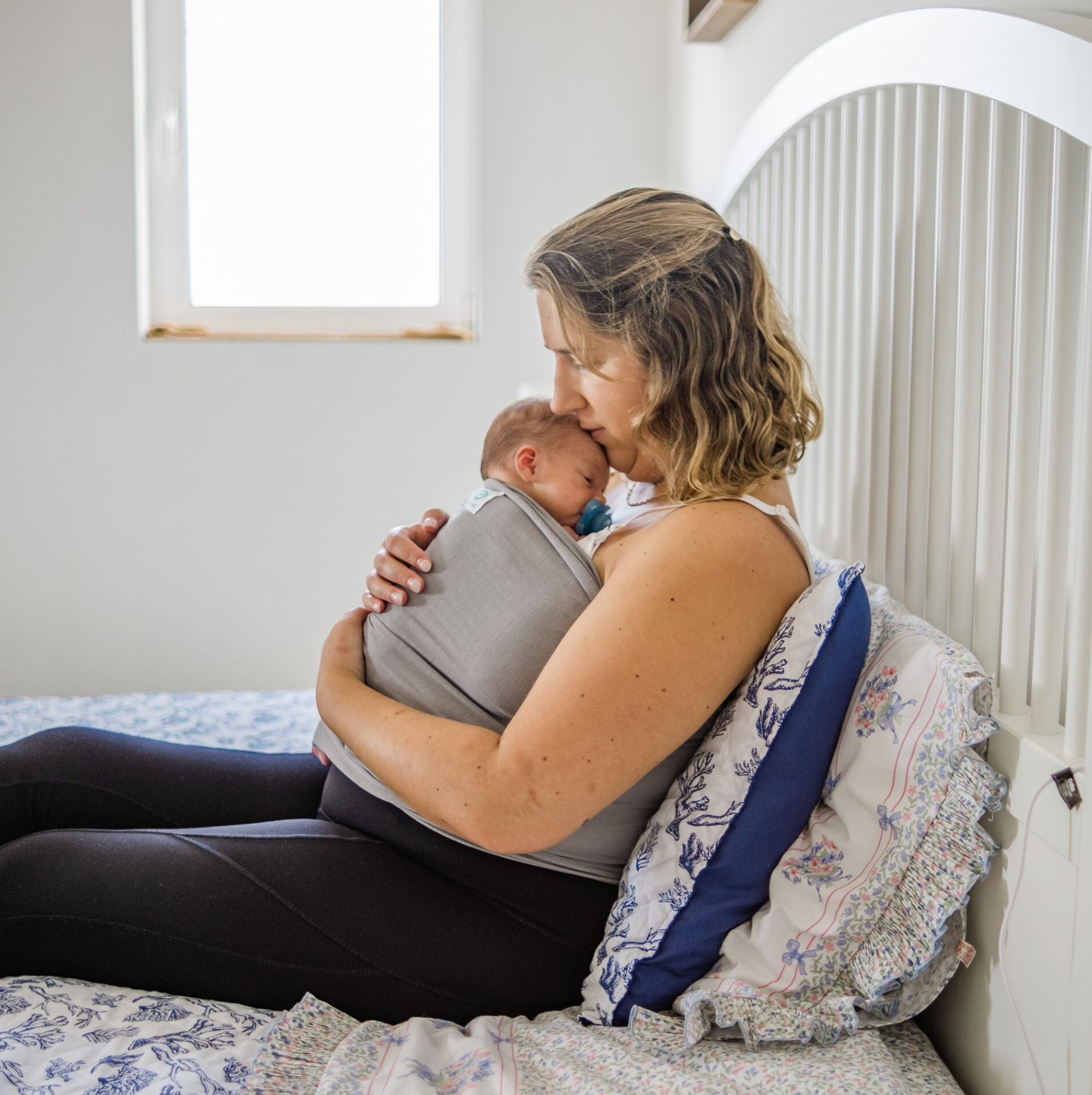 IGaroo Mulher sentada na cama a segurar bebé num porta-bebés cinzento