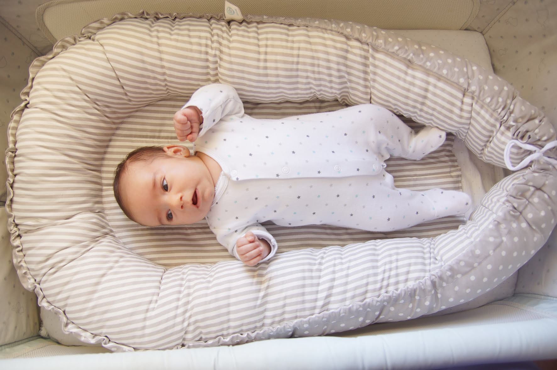 Ninho mix de padrões Bebé deitado num ninho de bebé acolchoado com padrão de riscas e bolinhas