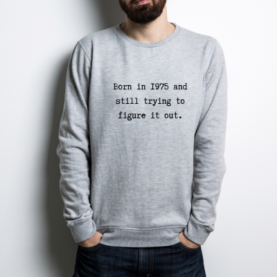 Camisola cinzenta com texto preto 'Born in 1975 and still trying to figure it out.'