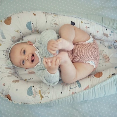 Bebé deitado em almofada tipo ninho com padrão de animais