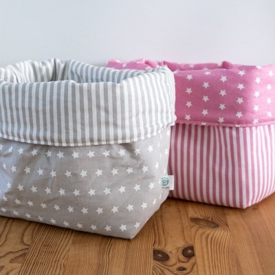 Dois cestos de tecido em padrões de estrelas e riscas, um bege e outro rosa, sobre mesa de madeira