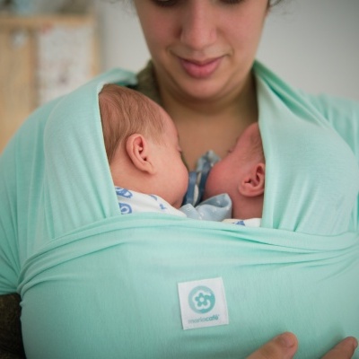 Mulher a usar suporte azul claro para dois bebés ao peito