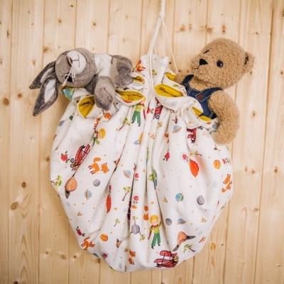 Saco de pano branco com padrão colorido e dois brinquedos de pelúcia pendurado na parede de madeira