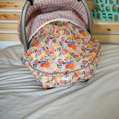 Cadeira de bebé com padrão floral colorido e interior xadrez rosa num ambiente com parede de madeira clara