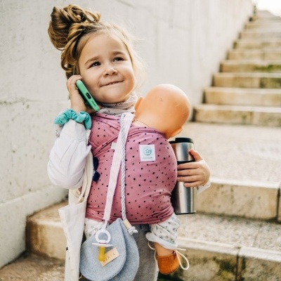 Criança com porta-bebés rosa carregando boneca em escadas de pedra