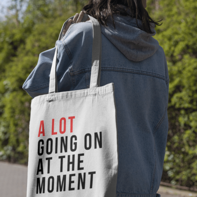 Mala tote branca com texto em vermelho e preto carregada por pessoa ao ar livre