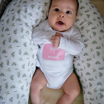 Bebé de 3 meses vestido com body branco e almofada de amamentação com padrão floral