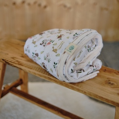 Manta branca com padrão de coelhos e plantas sobre bancada de madeira