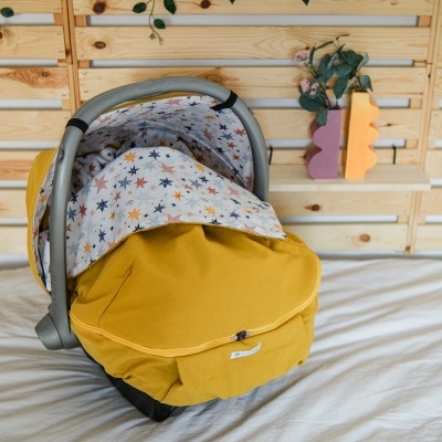 Cadeira auto bebé amarela com padrão de estrelas coloridas em ambiente interior com parede de madeira