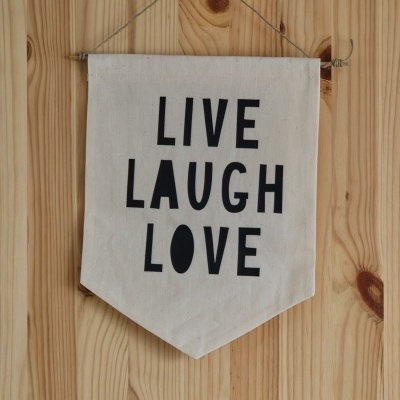 Bandeira decorativa com texto LIVE LAUGH LOVE pendurada numa parede de madeira