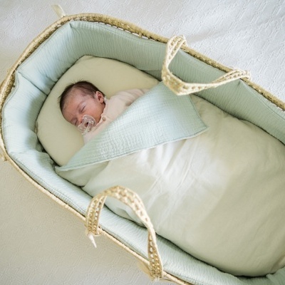Bebé adormecido numa alcofa com forro verde-água e cobertor branco
