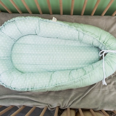 Ninho de bebé verde claro com bolinhas brancas e laterais acolchoadas numa cama de grades de madeira clara