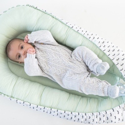 Bebé deitado num ninho para bebés com tecido verde e branco com padrão preto