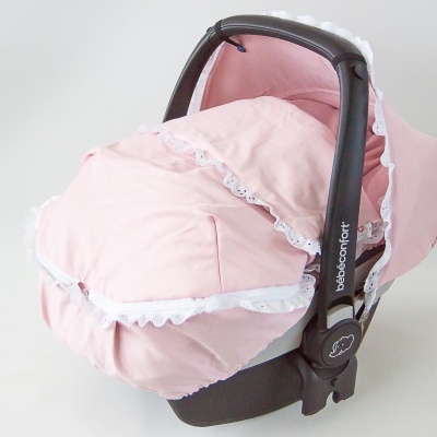 Cadeirinha para bebé com capa rosa e detalhes em renda branca numa superfície branca.
